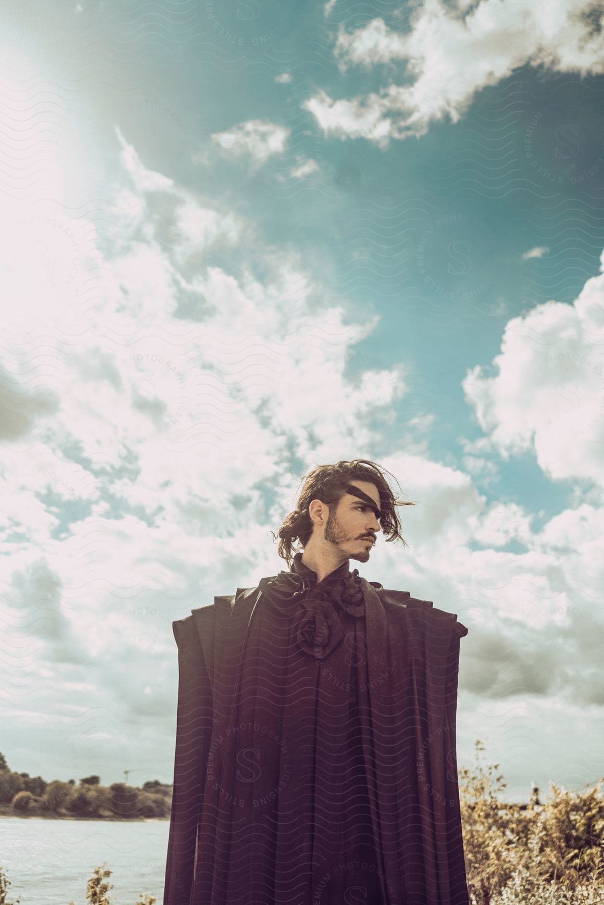 Stock photo of man models clothes standing on shore on cloudy day.