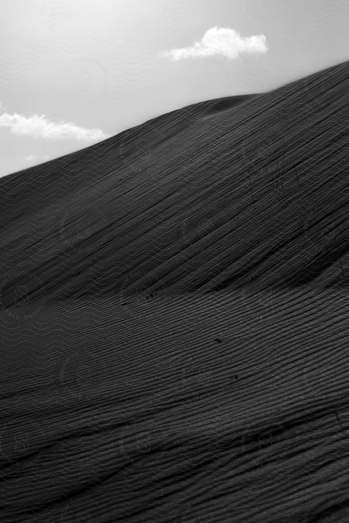 Desert sand covers slopes under a cloudy sky on a sunny day.