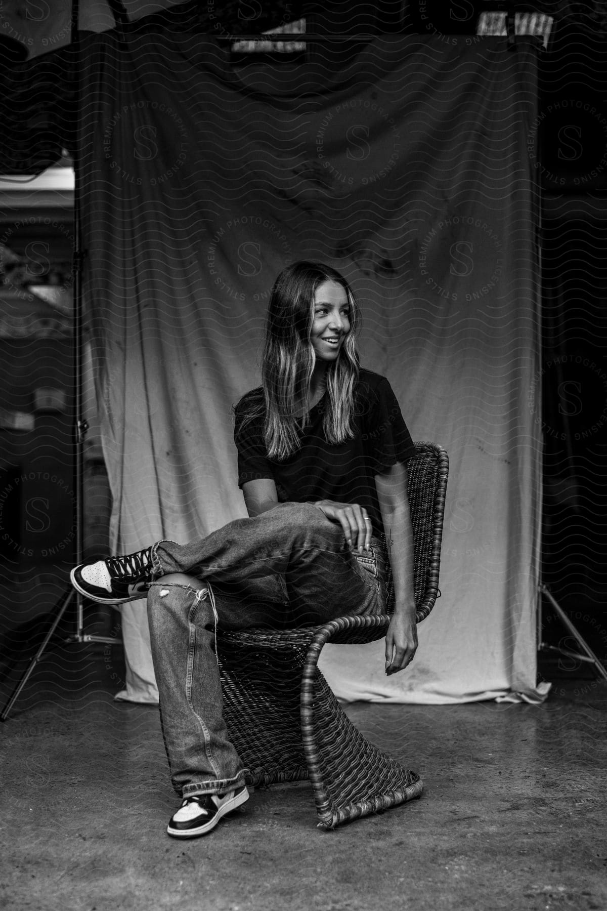 A woman with brown hair, dressed in a black t-shirt and jeans, sits in a wooden chair, laughing heartily