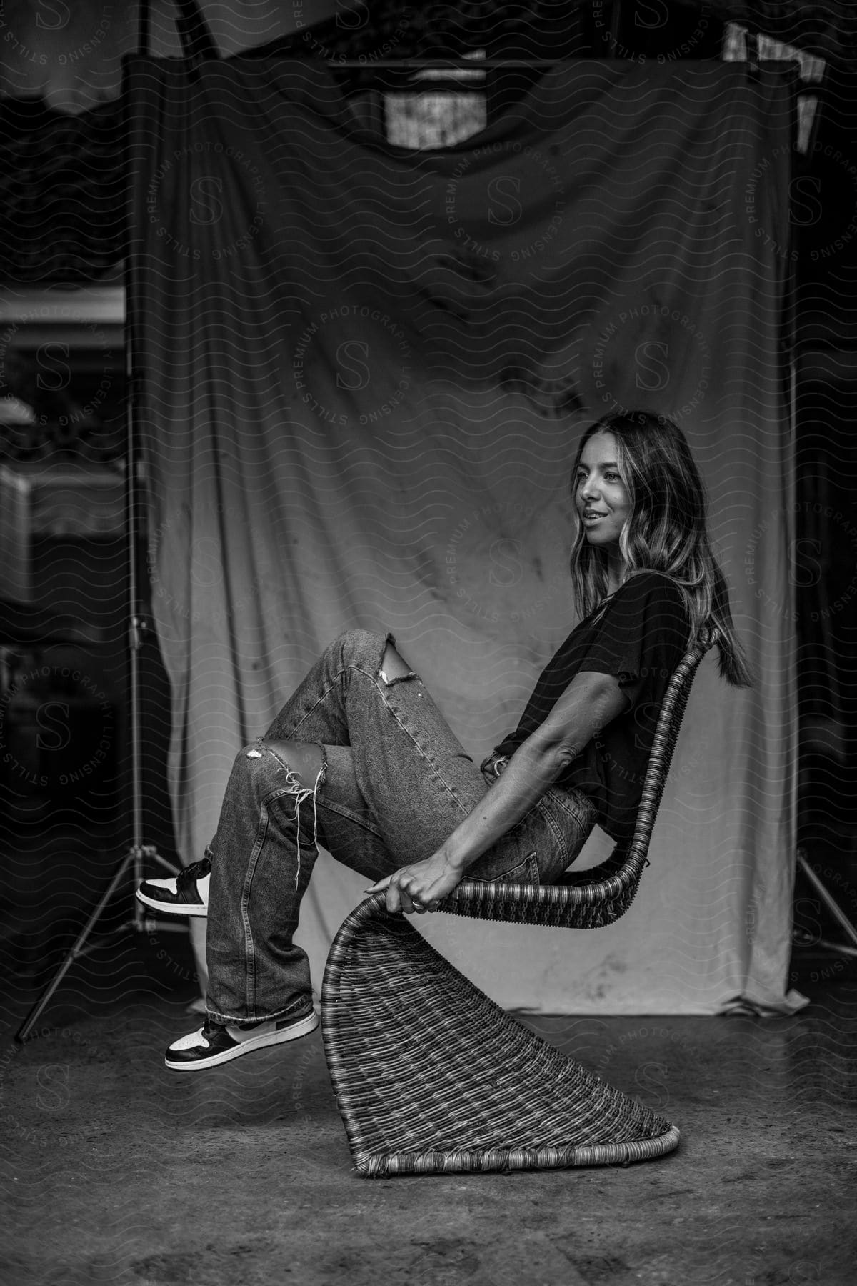 Woman poses on curved wicker chair in photo studio.