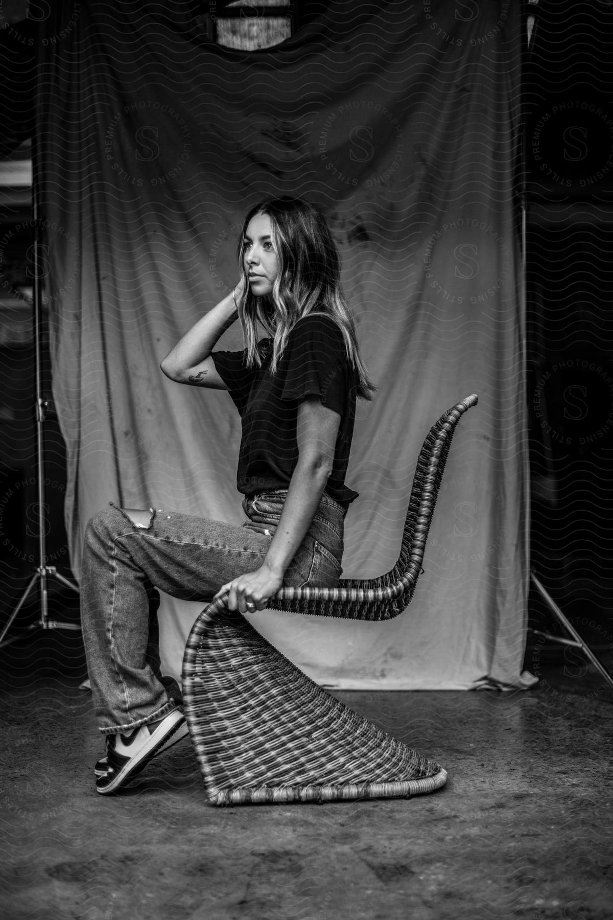 A young woman with paint on her arm sits on a rattan woven chair.