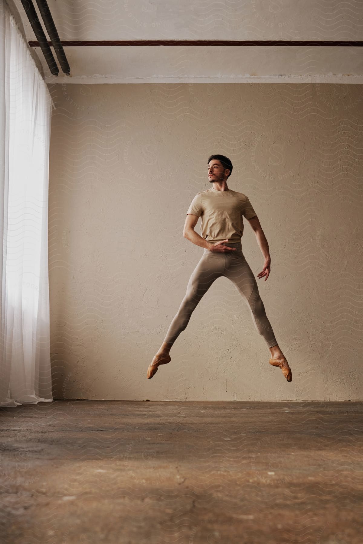 Male dancer leaps upward in an empty curtained room.