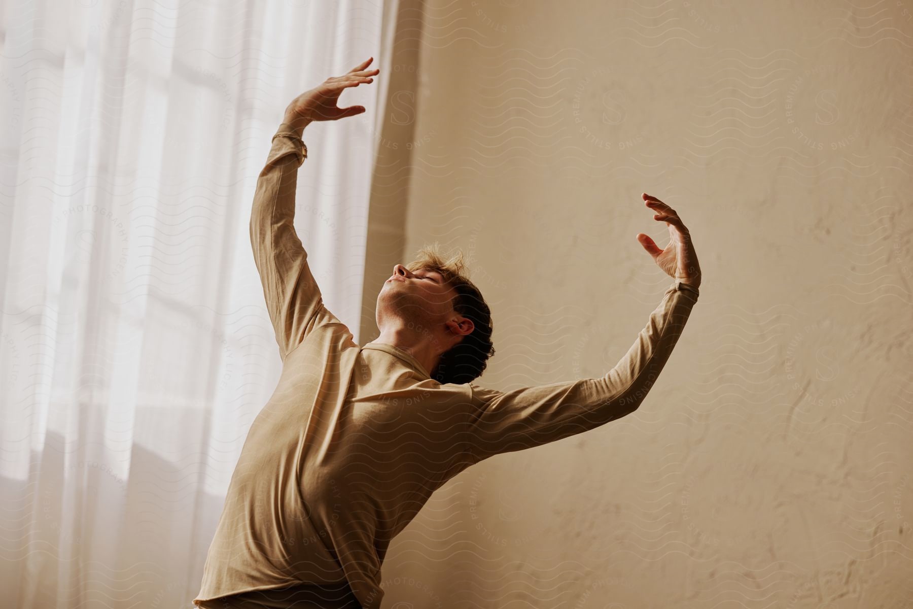 A man in a brown sweatshirt dances in front of curtains and a brown wall