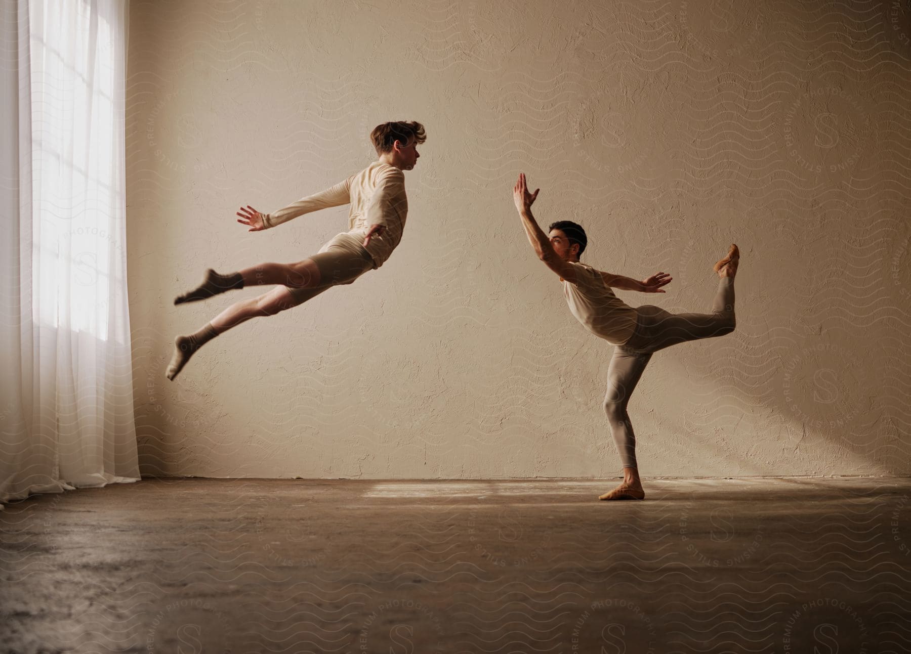 Male dancers practice routine in empty curtained room.