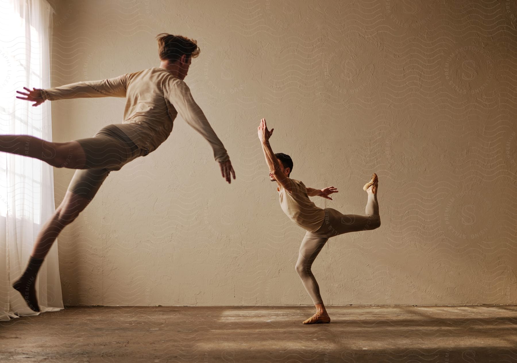 Two young men ballet dancing, with one of them leaping into the air.