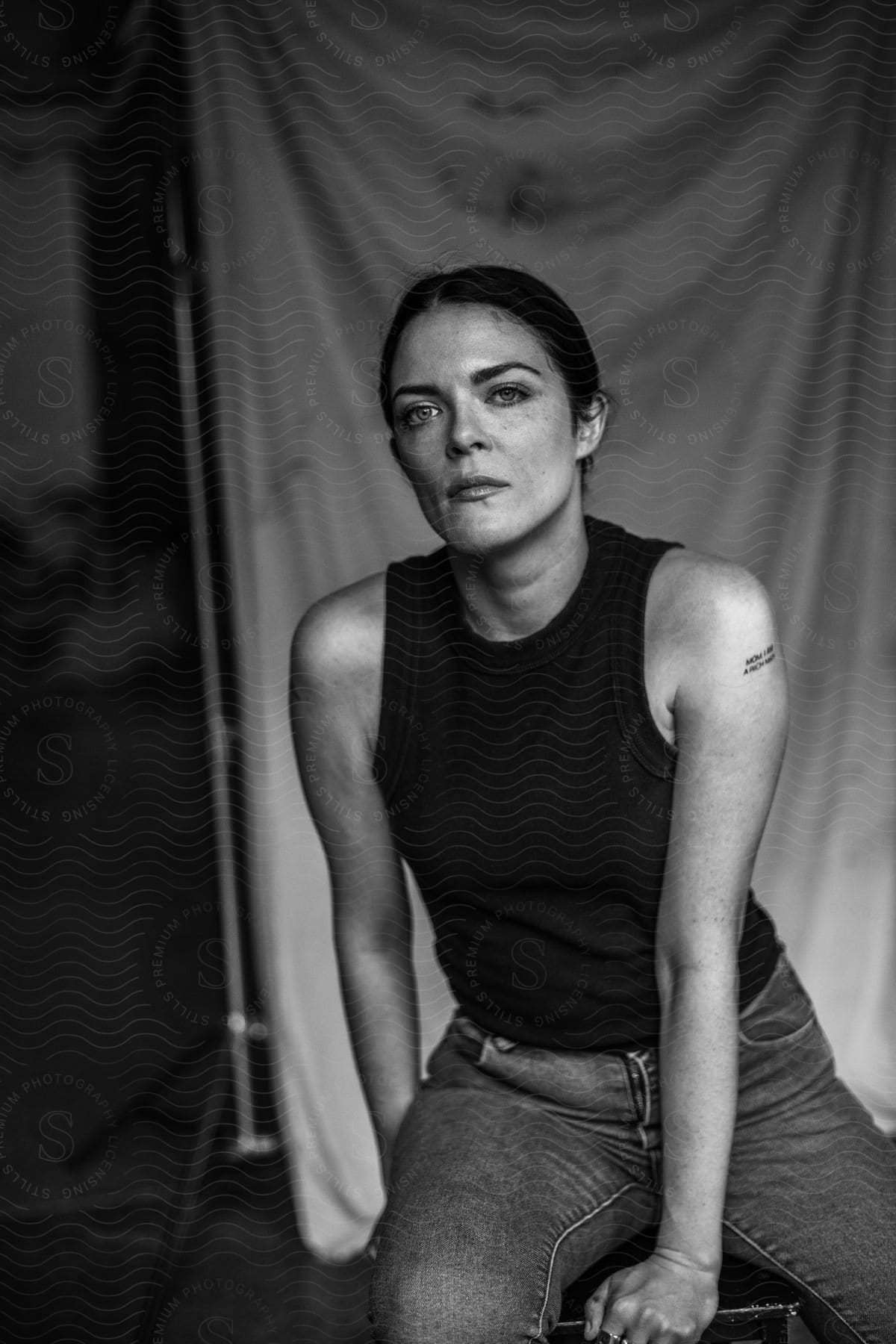 Woman with black top tattoo and jeans sits on a stool