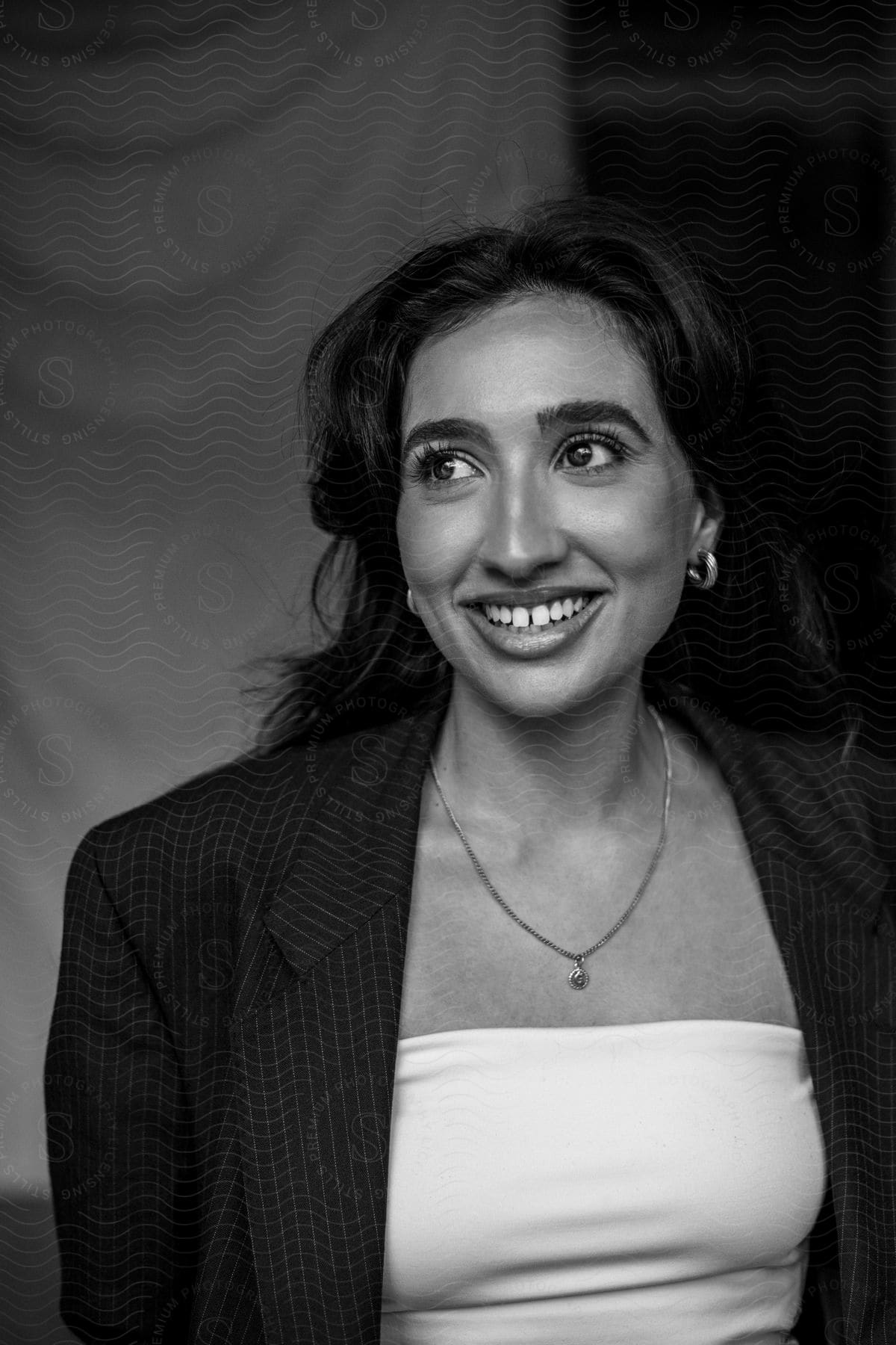 A woman is wearing a pinstripe blazer as she looks to her side and smiles