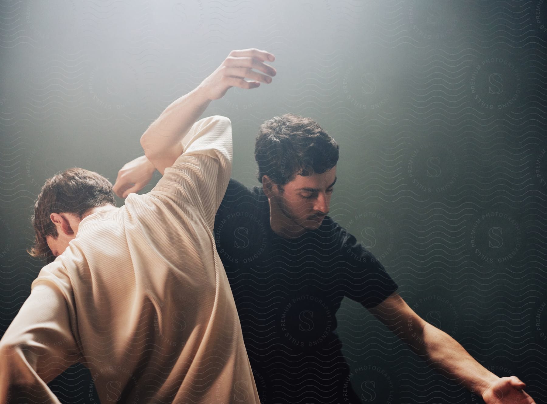 Two men perform dance on stage under a theater spotlight.