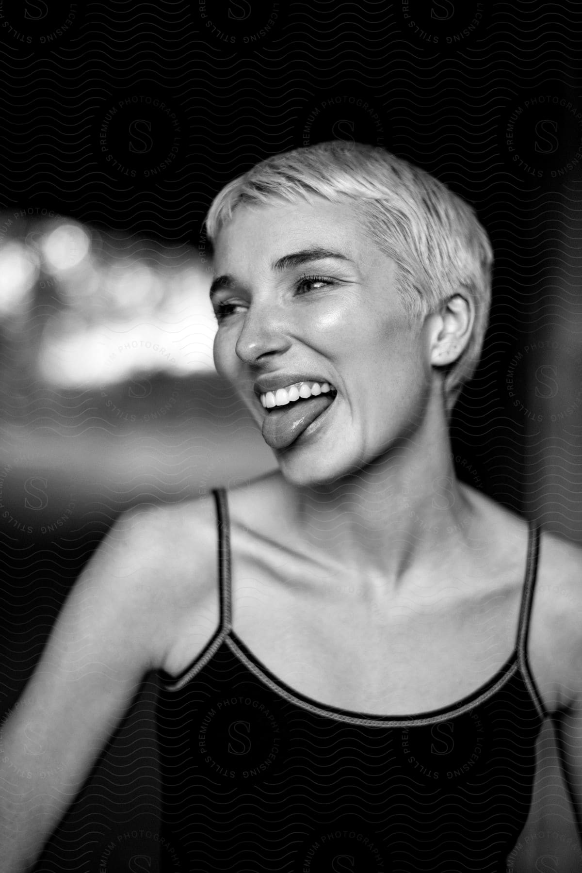 A Woman With Short Hair With Her Tongue Out While Smiling And Looking To The Side In Monochromatic Tones