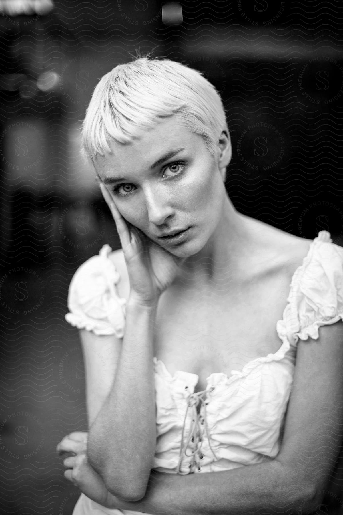 A Woman With Short Blonde Hair Stands With Her Hand On Her Face As Her Head Is Tilted