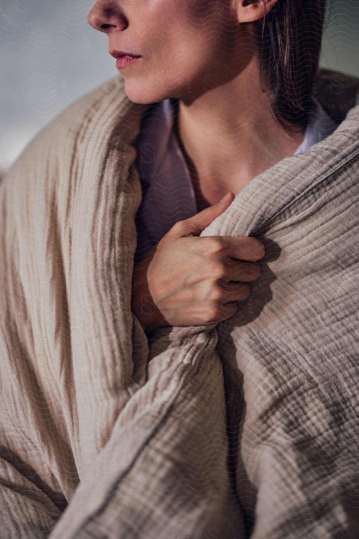 A woman holds a blanket wrapped around her shoulders with her hand as she looks to her side