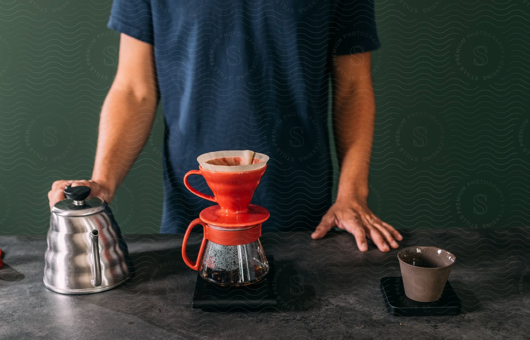 Hands of a man on a kettle while coffee is being filtered.