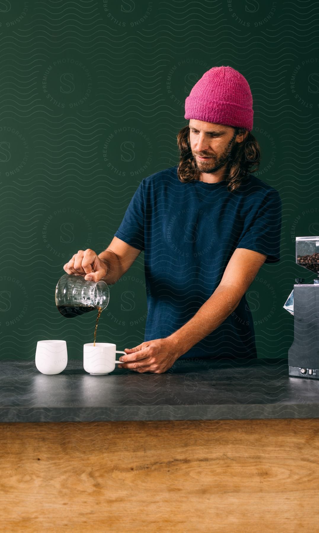 A man pours coffee into a white mug on a grey countertop.