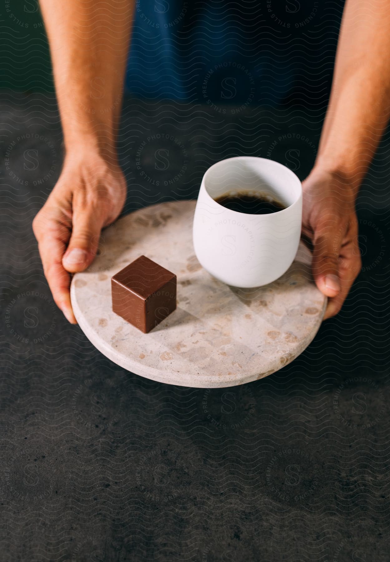 A man serving coffee in a white cup and a chocolate on a plate.