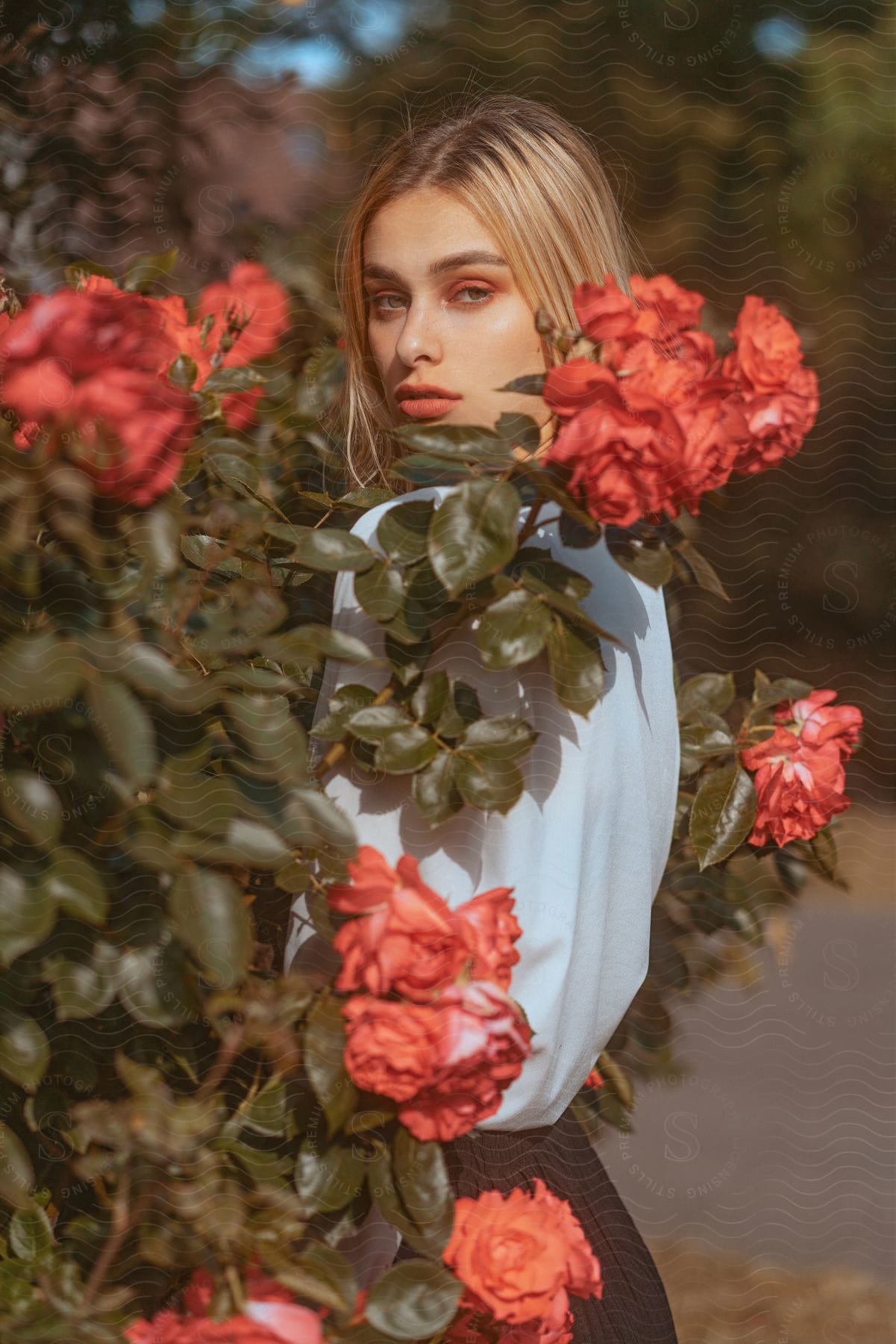 A blonde woman is standing in a flower garden as she turns and looks at the camera