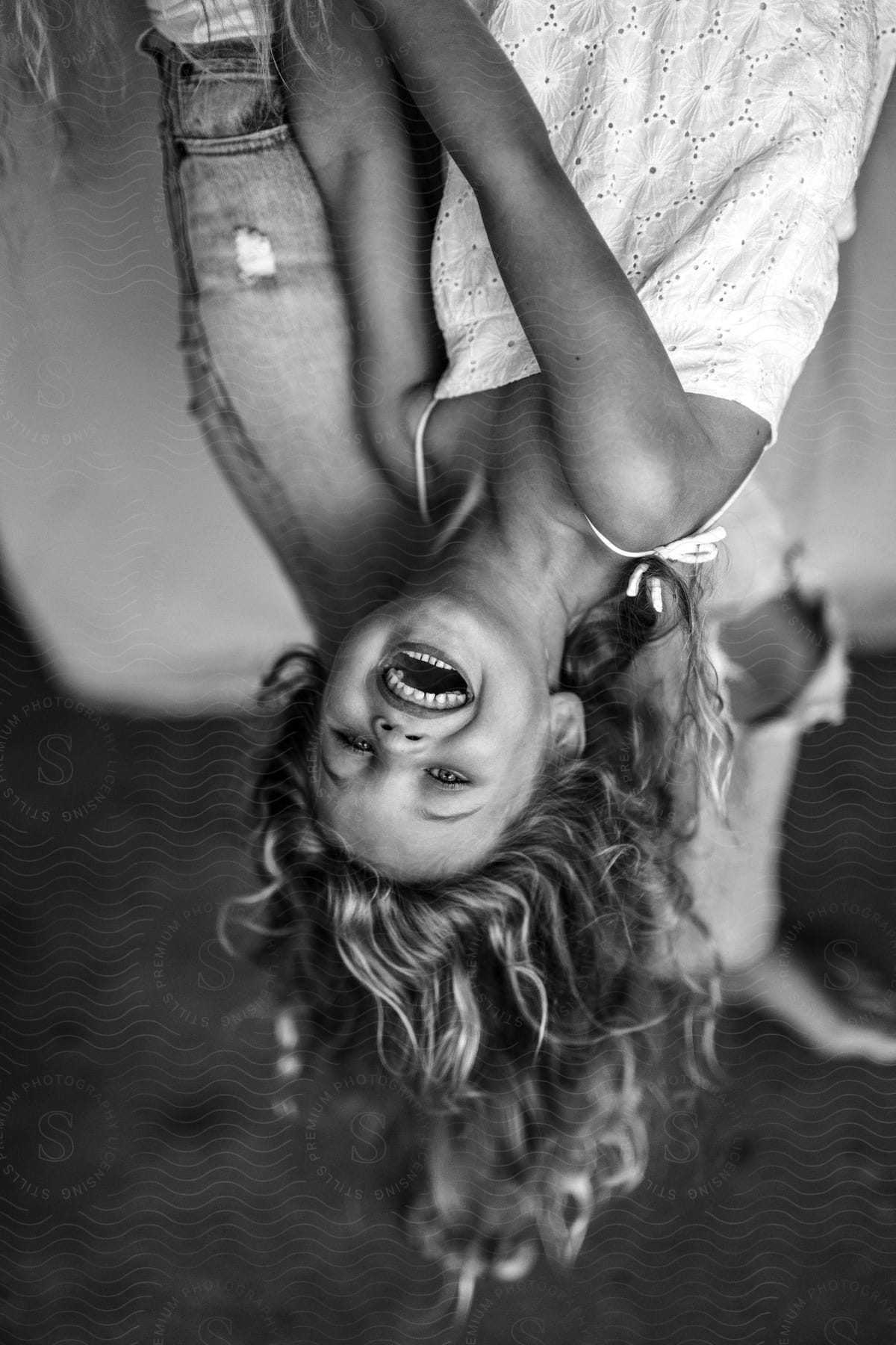 A little girl smiles and laughs as she hangs upside down with an adult behind her.