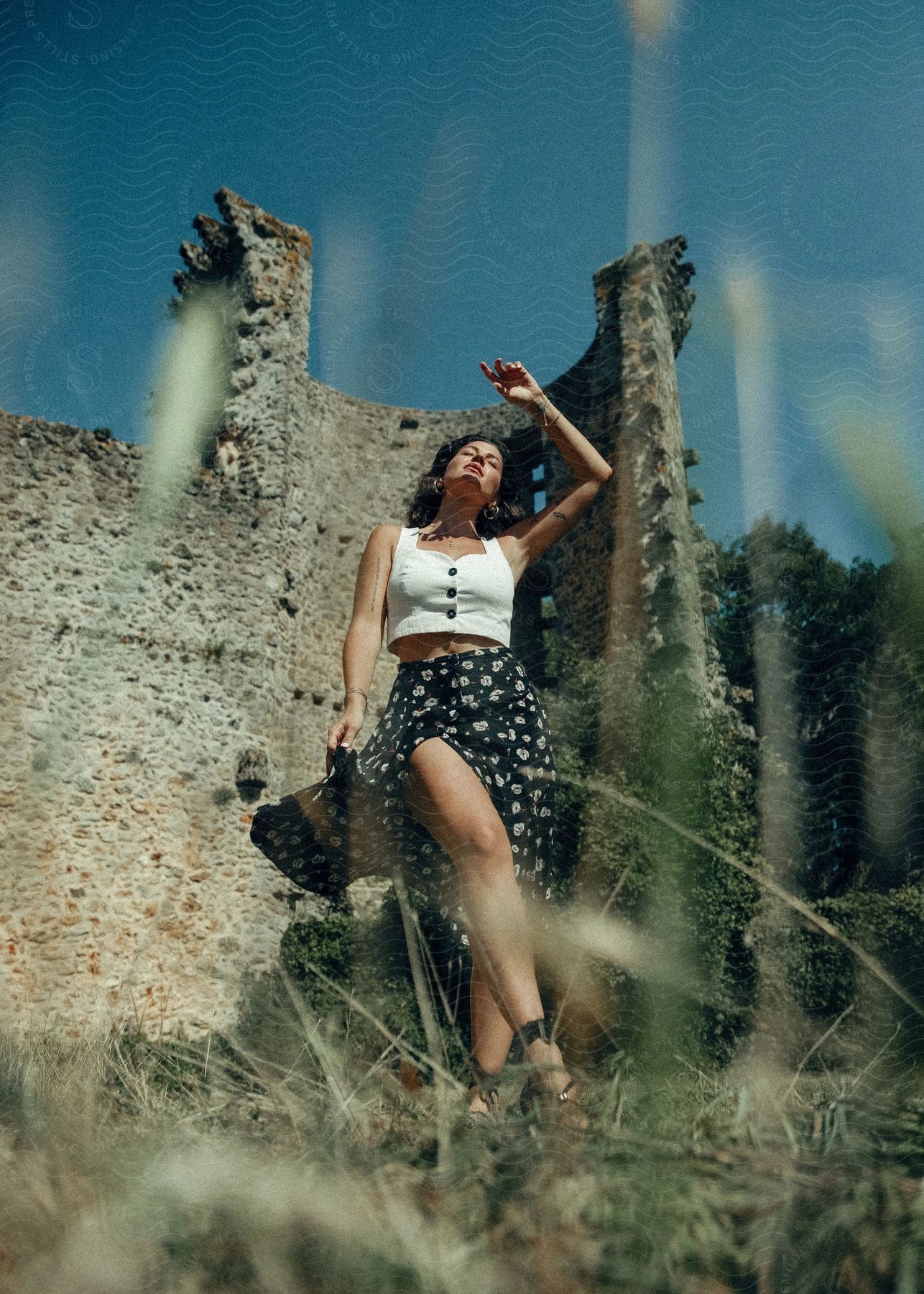 Fashion model poses against  wall of ruined building on a sunny day.