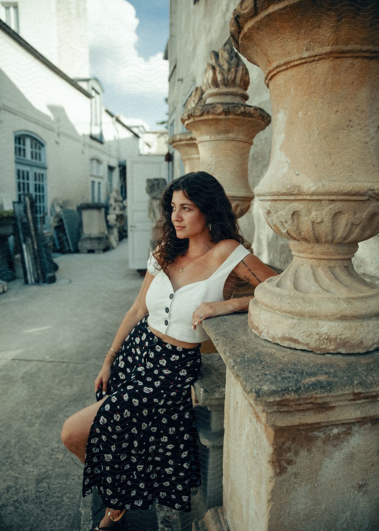 A woman in a skirt and white shirt is leaning against the wall and looking to her right.