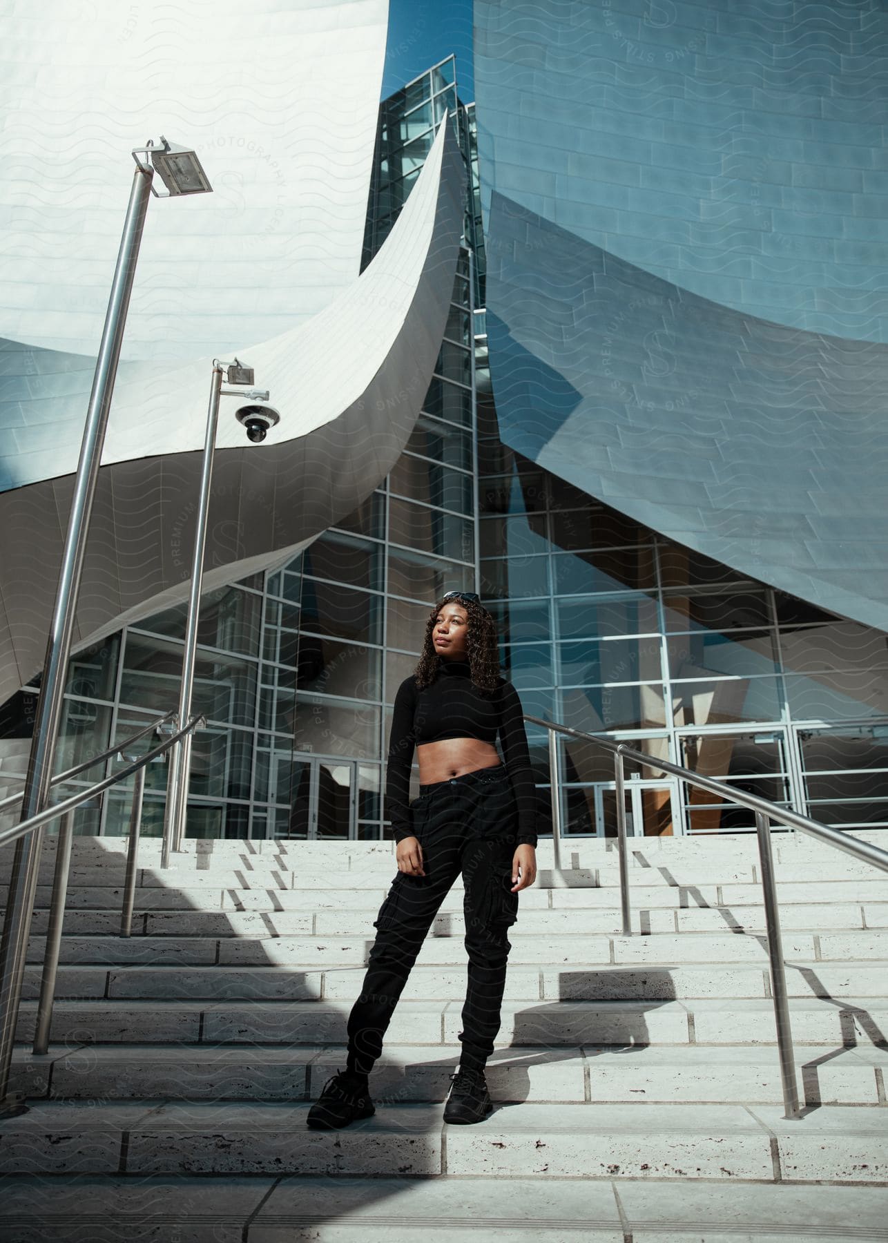 A woman wearing black pants and a long sleeve halter top is standing on steps outside of a building