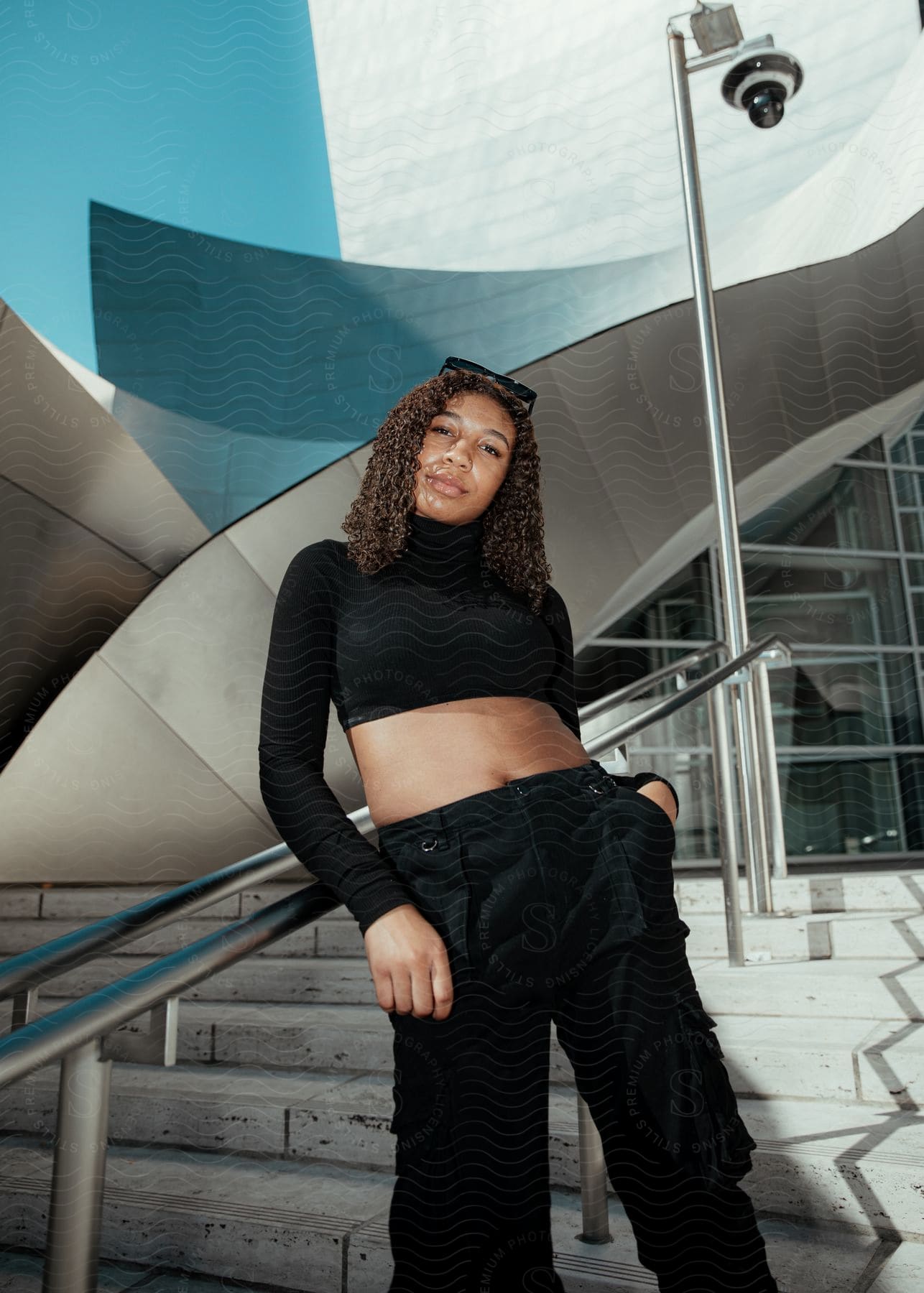 Young woman crouched on a staircase railing of a building, modeling in an all-black outfit.