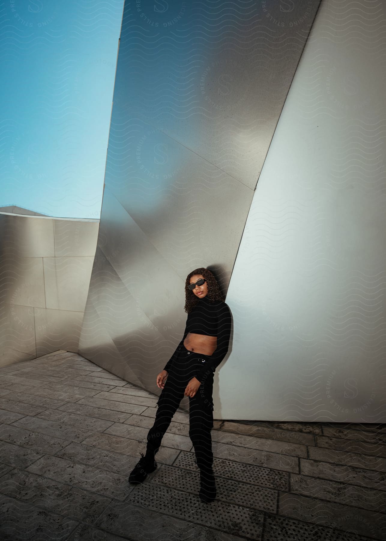 young lady in black crop top, jean, and shoe, leaning against the wall
