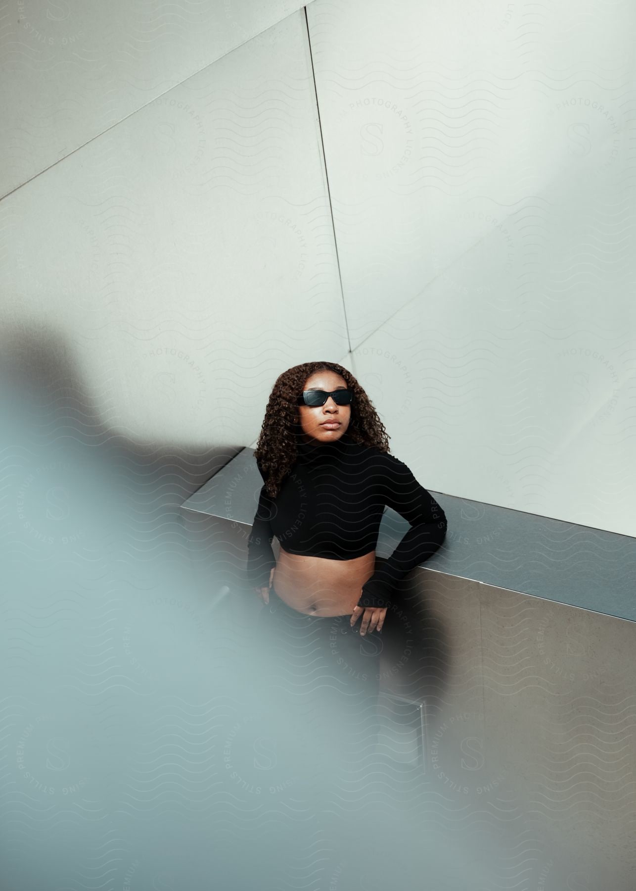 Woman leaning against a metal wall and modeling in an all-black outfit.