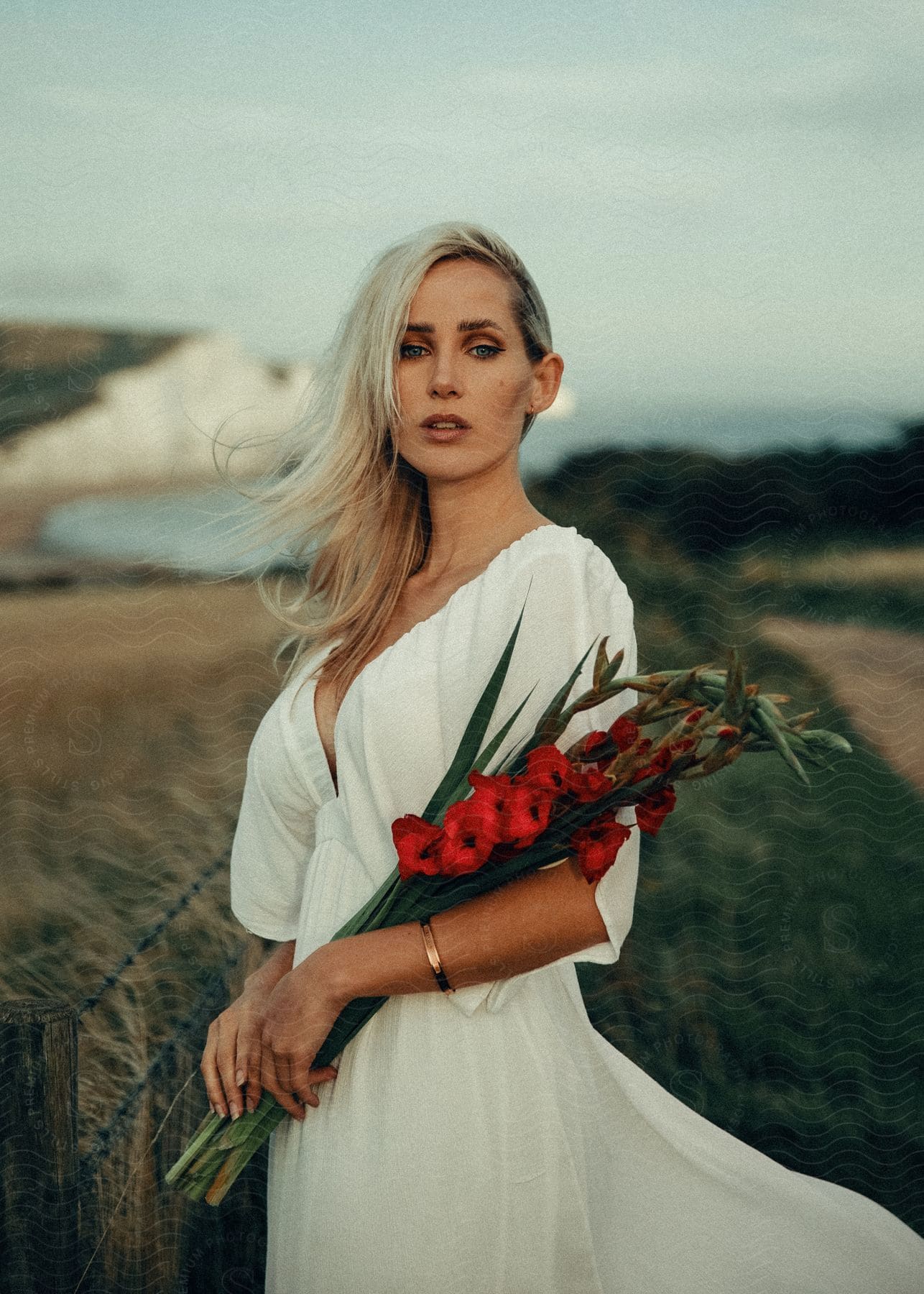 Woman in white dress holding red flowers with chalk cliffs in background