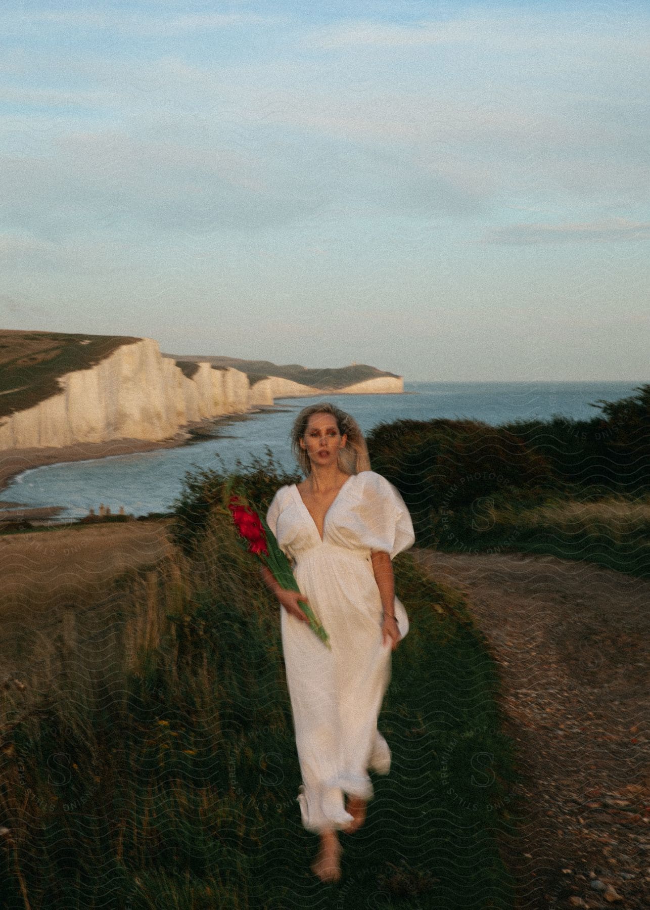 Stock photo of a woman is walking in the grass near a beach.