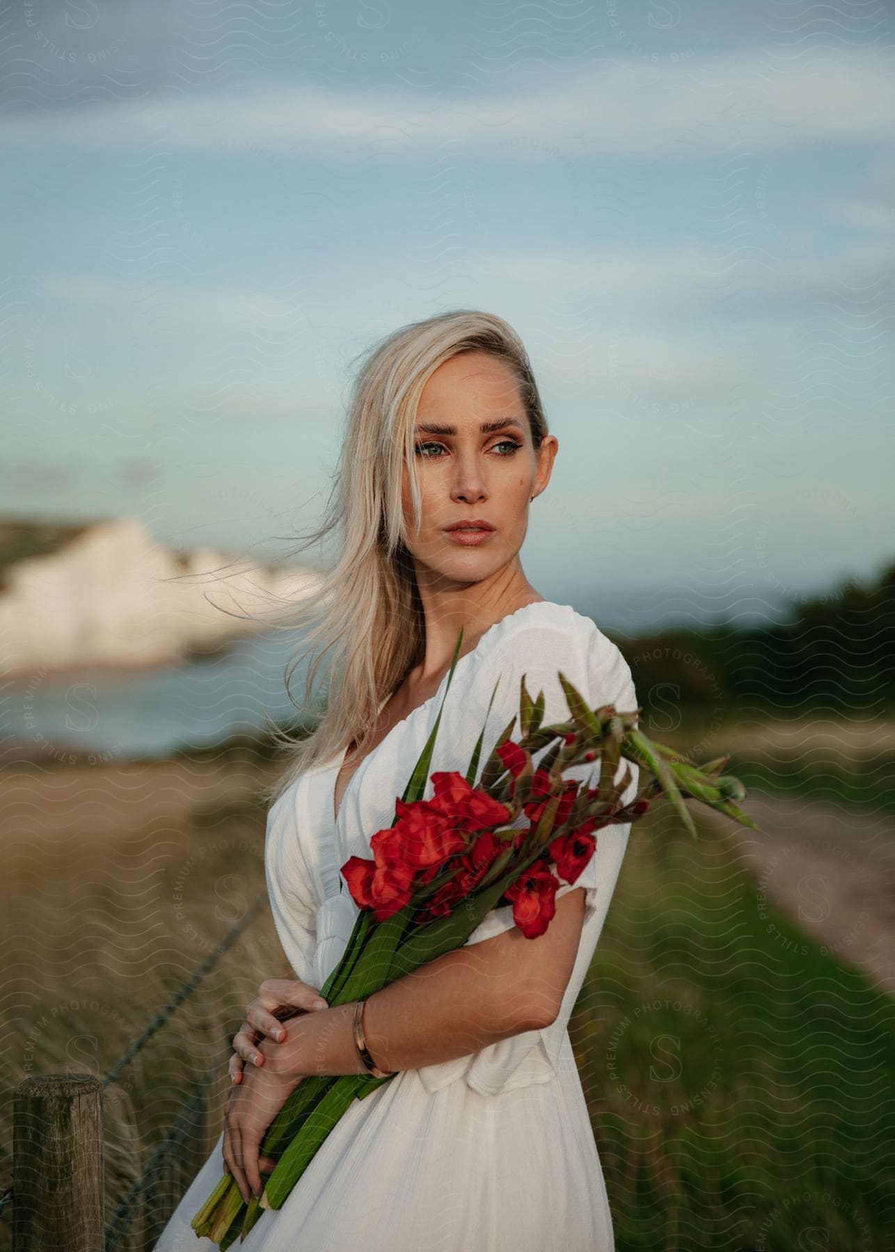 Woman posing in a white dress with a bouquet of red orchids.