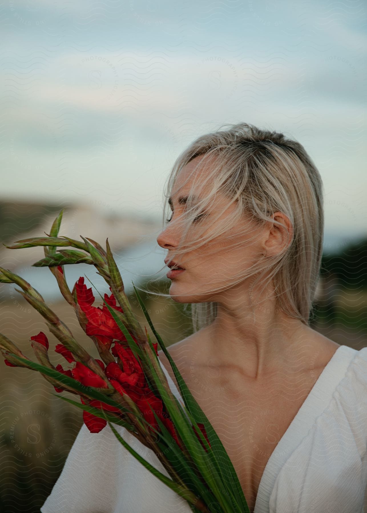 A woman is standing holding a bouquet of flowers as her long blonde hair blows across her face