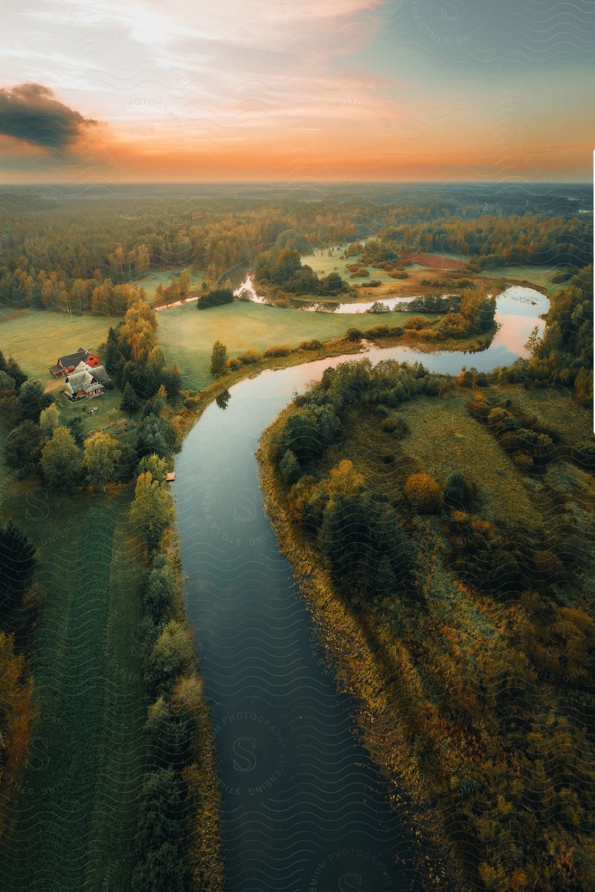 A river with reflective water that runs through a forest with some houses.