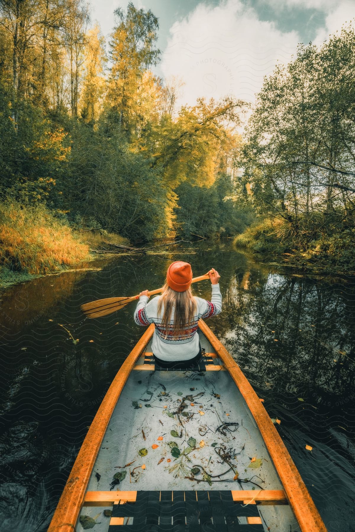 View from the back of a blonde woman paddling a canoe on a lake surrounded by trees.