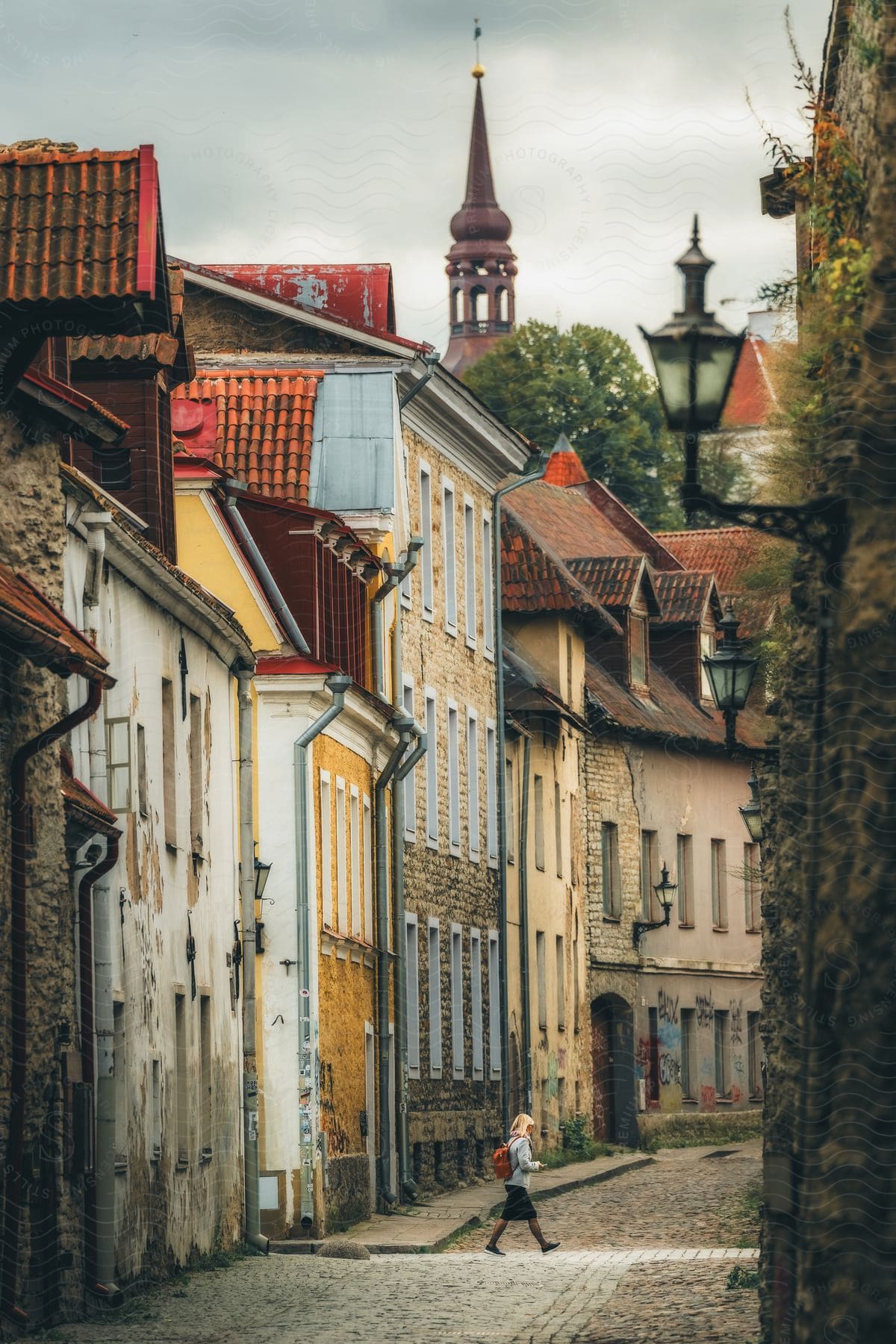 A woman walks on a cobblestone street in Estonia near medieval buildings