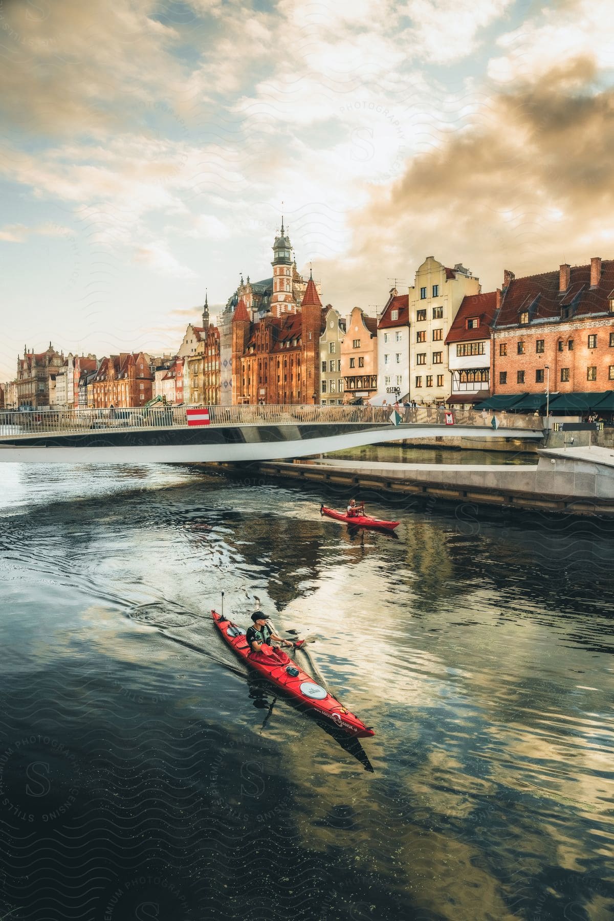 Two people using kayaks in a river next to a city.