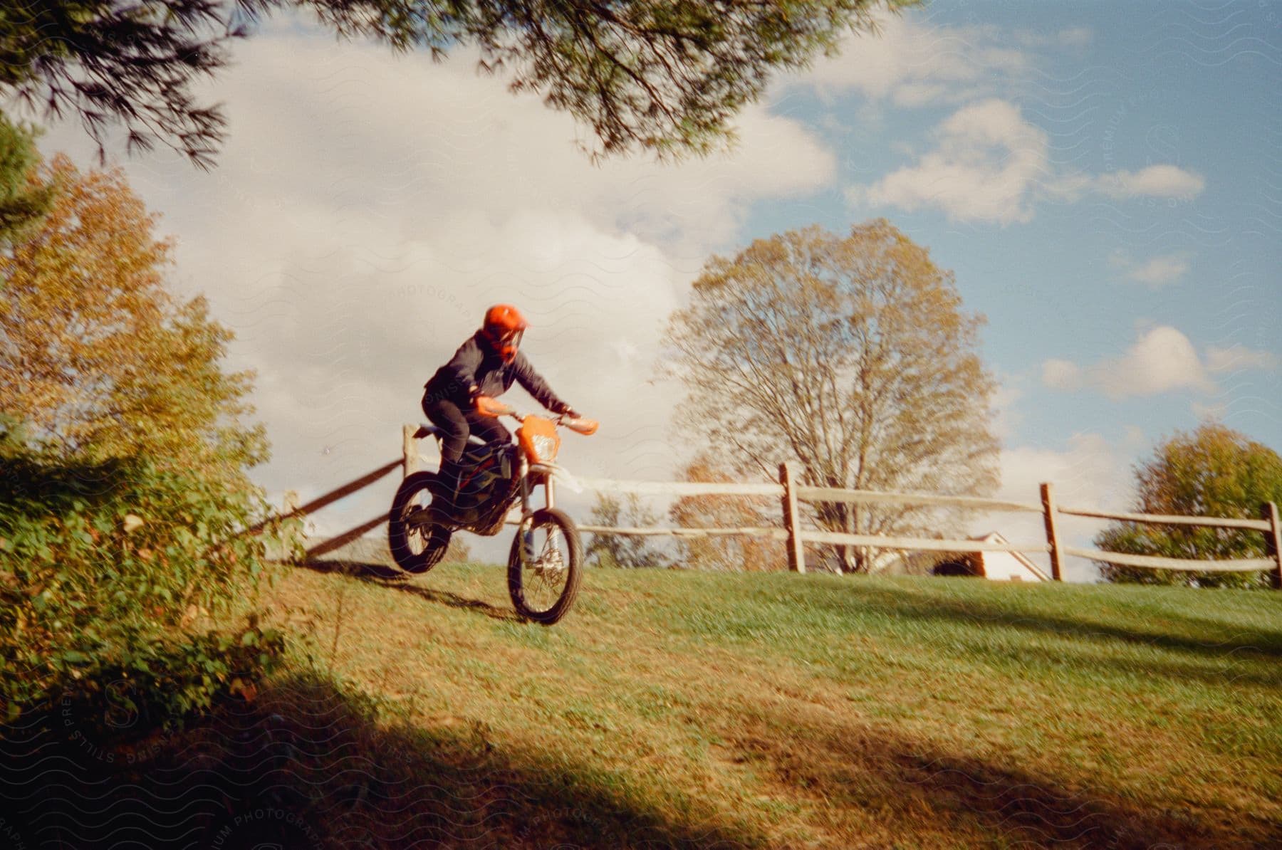 A person rides a motorcycle down a grassy hill on an autumn day.