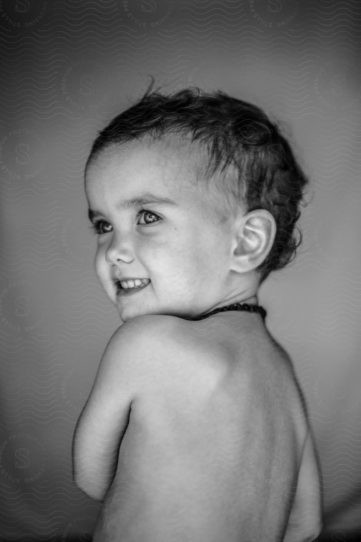 A toddler boy looks over his shoulder, wearing a smile.