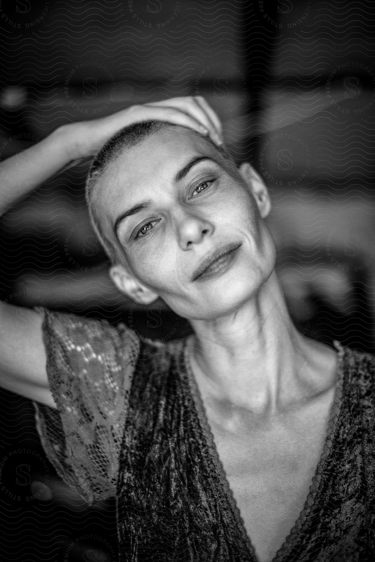 Portrait of a woman with short shaved hair, one hand on her head, and a happy facial expression.