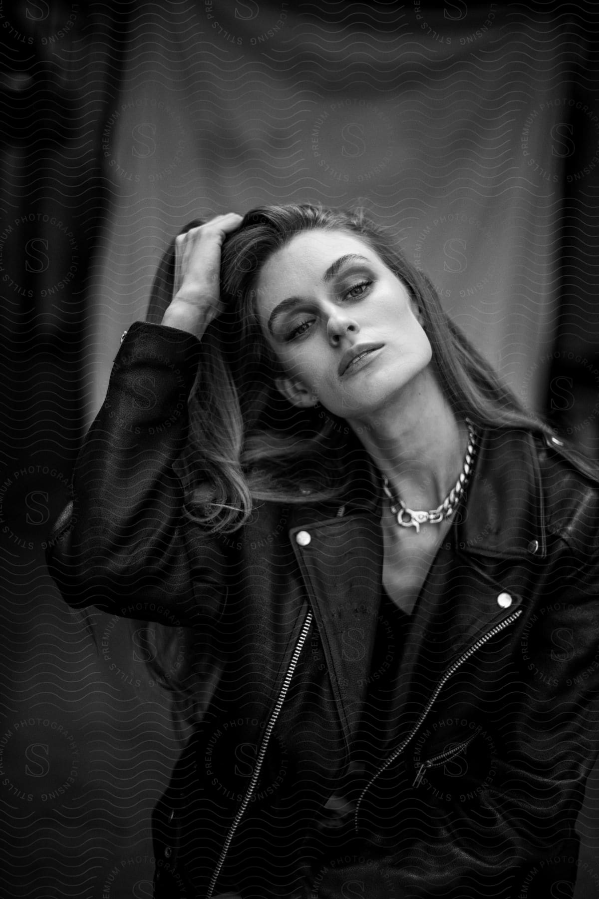 A young woman models a black leather jacket and a thick, chain necklace.