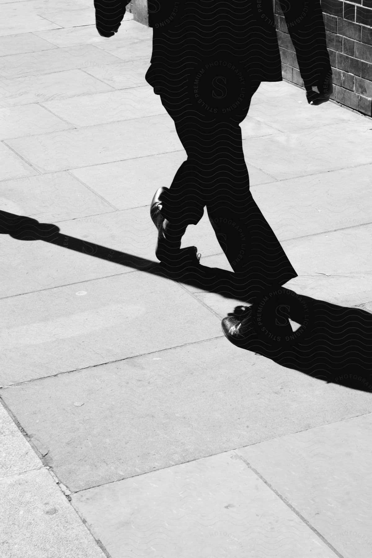 Man wearing suit casts shadow as he walks along pavement next to building.