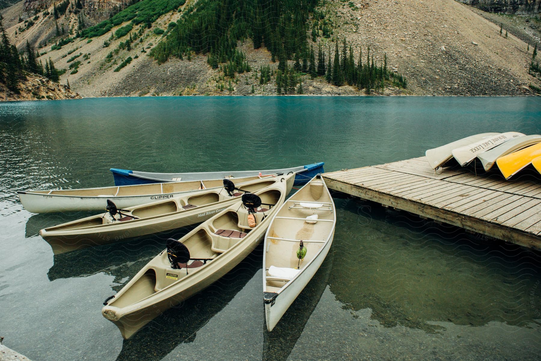 Canoes In The Water Are Tied To The Dock With Mountains Across The River