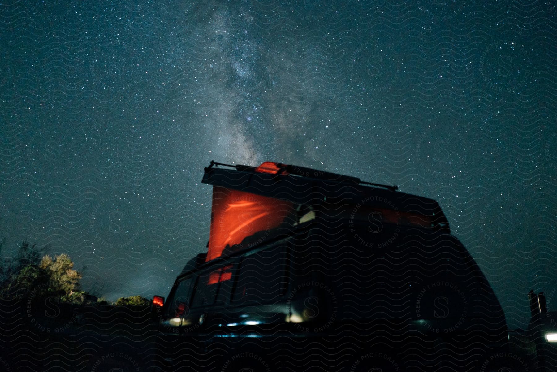 Light glows from inside a camper van sitting under the stars of the Milky Way