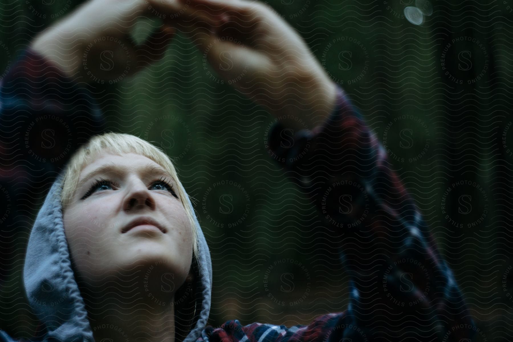 Blonde woman with red jacket looks up in the forest