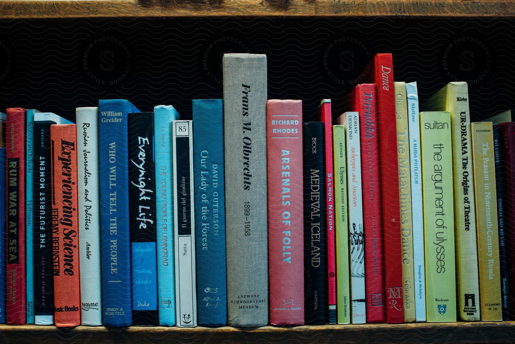 A bookshelf with several side books of different sizes and thicknesses and colors.