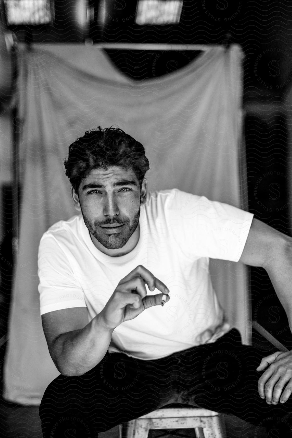 brunette male wearing white t-shirt sits and smokes posing