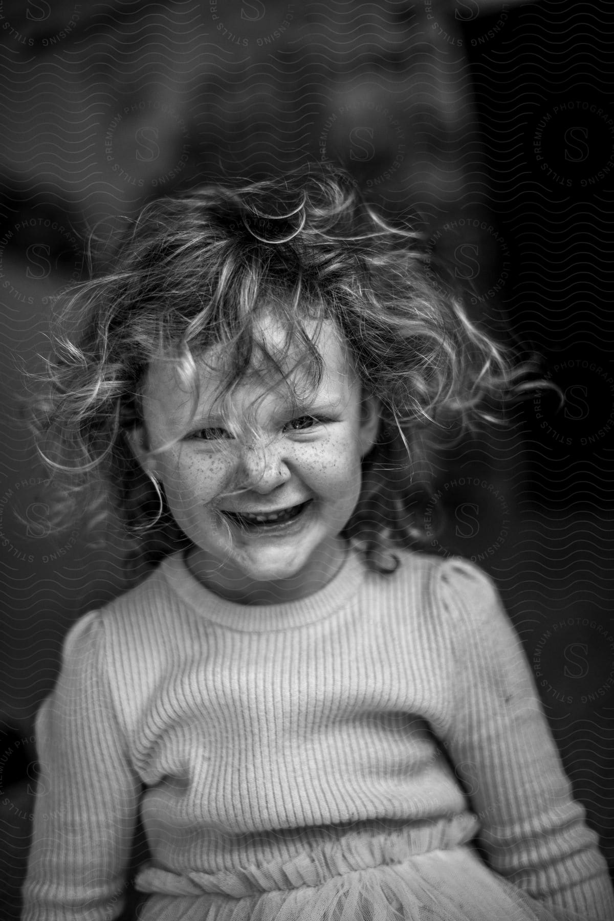 A little girl smiles and laughs as her wavy hair blows in her face