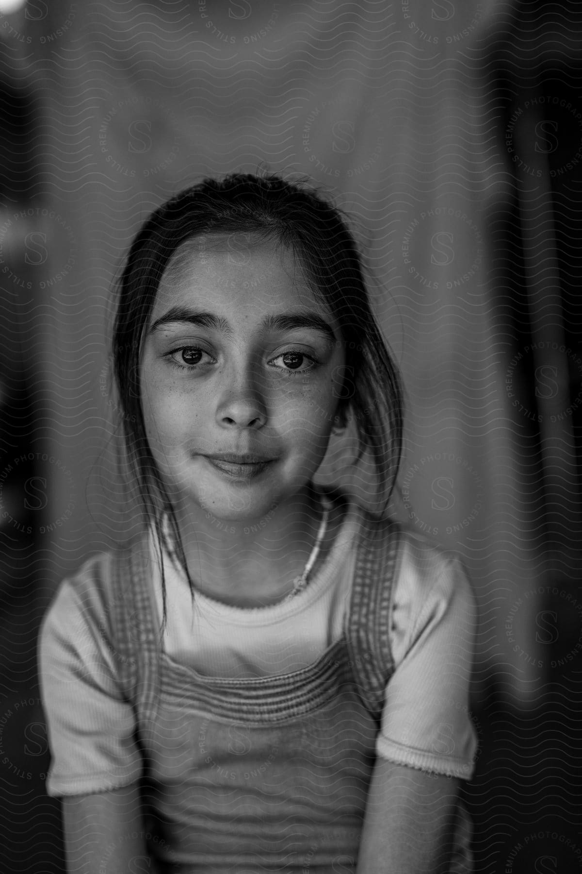 A girl wearing overalls and a t-shirt while displaying a contemplative attitude.