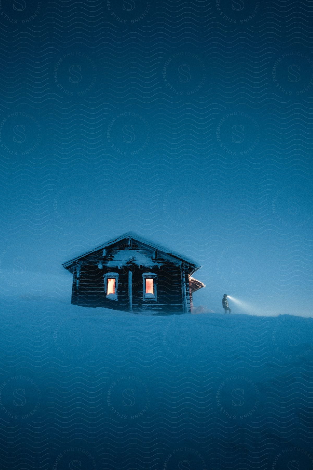 Cabin in the midst of fog and snow with a person outside wearing a headlamp.