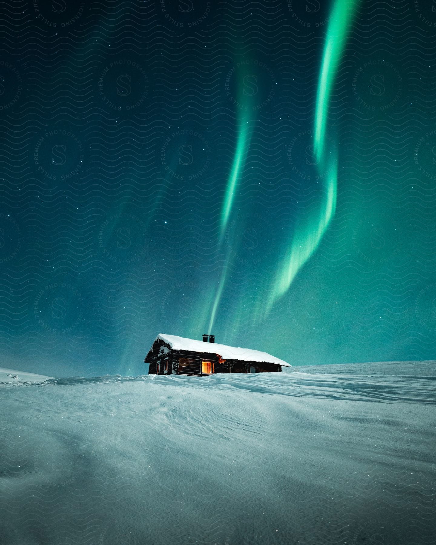 Stock photo of a snow-covered cabin with northern lights in the sky.