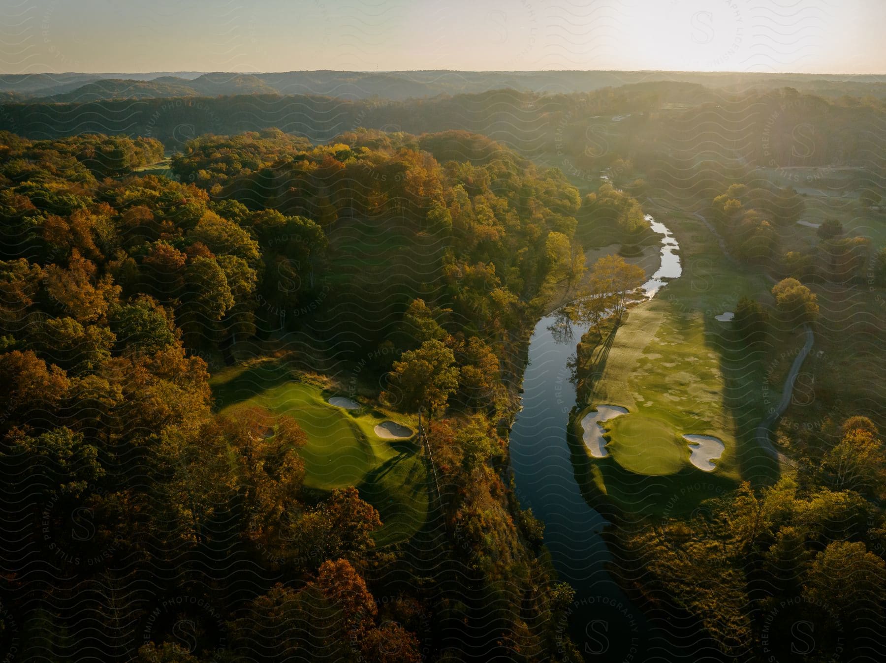 A river runs between golf courses surrounded by a forest of trees in fall colors