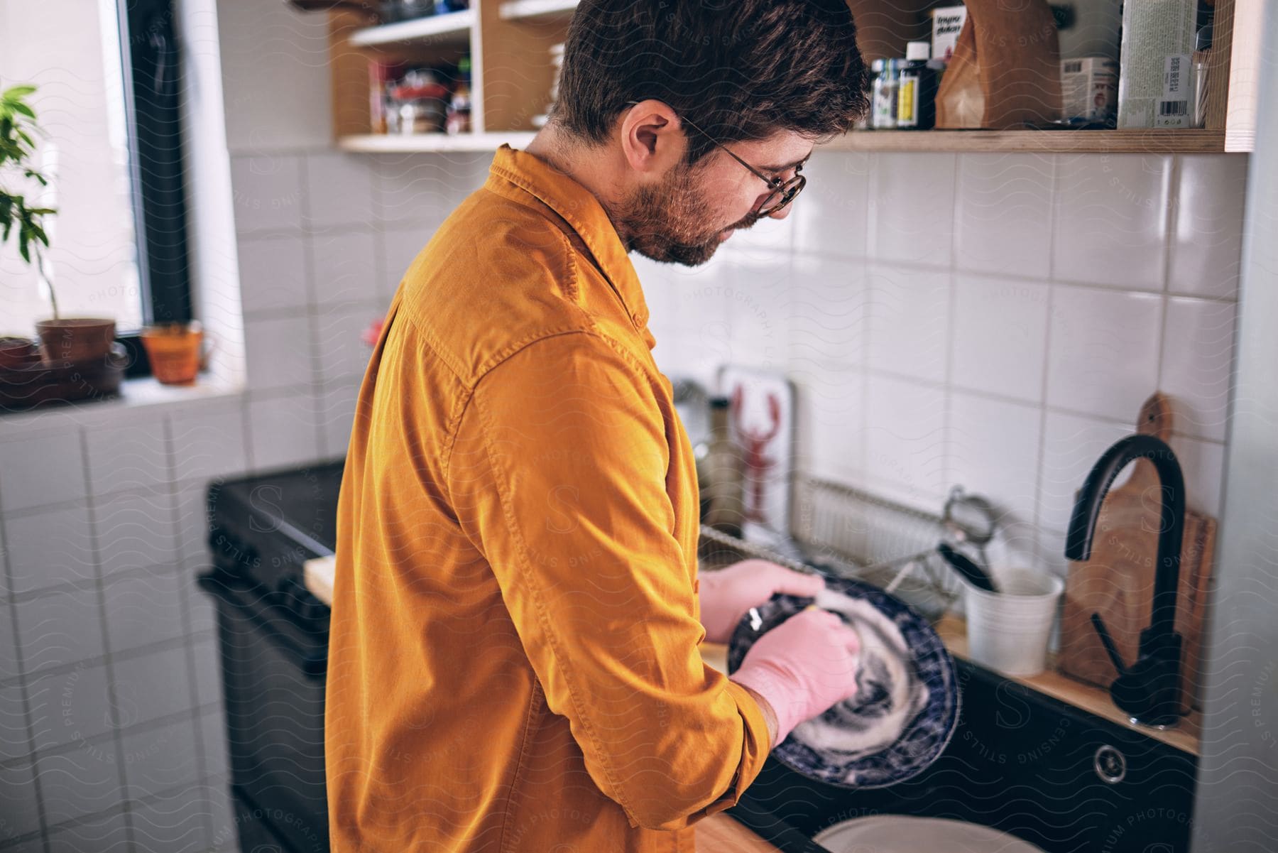 A man in a dark yellow shirt hand washing dishes.